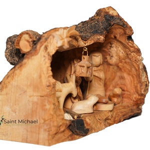 May include: A wooden nativity scene carved from olive wood. The scene is set inside a hollowed-out piece of wood, with the figures of Mary, Joseph, and the baby Jesus. There is also a donkey and a sheep in the scene.