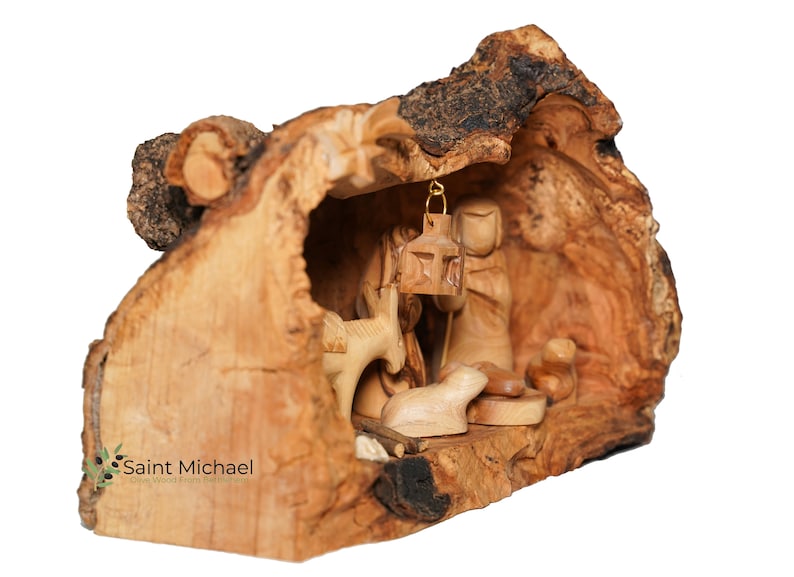 May include: A wooden nativity scene carved from olive wood. The scene is set inside a hollowed-out piece of wood, with the figures of Mary, Joseph, and the baby Jesus. There is also a donkey and a sheep in the scene.
