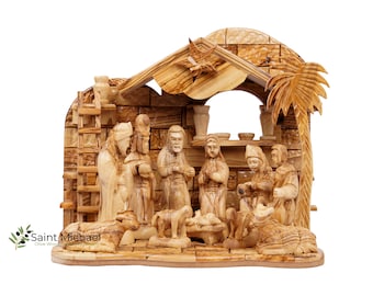 Può includere: Un presepe in legno d'olivo intagliato a mano con una rappresentazione dettagliata della Sacra Famiglia, pastori e animali. La scena è ambientata in una stalla con tetto di paglia e una palma.