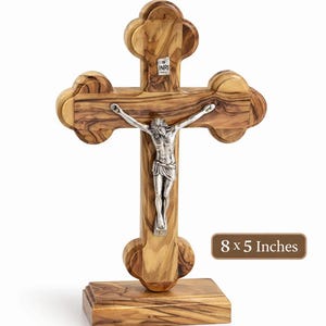May include: Hand-carved wooden cross with a silver figure of Jesus. The cross is 8 x 5 inches and is mounted on a wooden base. The text "Hand Carved in Bethlehem" is at the top.