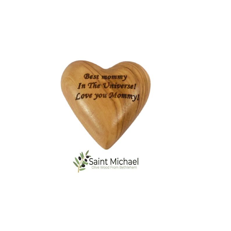 May include: A heart-shaped olive wood carving with the inscription "Best mommy In The Universe! Love you Mommy!". The wood has a warm, natural tone. The Saint Michael logo is at the bottom.