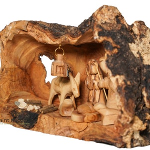 May include: A hand-carved nativity scene set inside a hollowed-out olive wood log. The scene features a donkey, a shepherd, and a small fire.