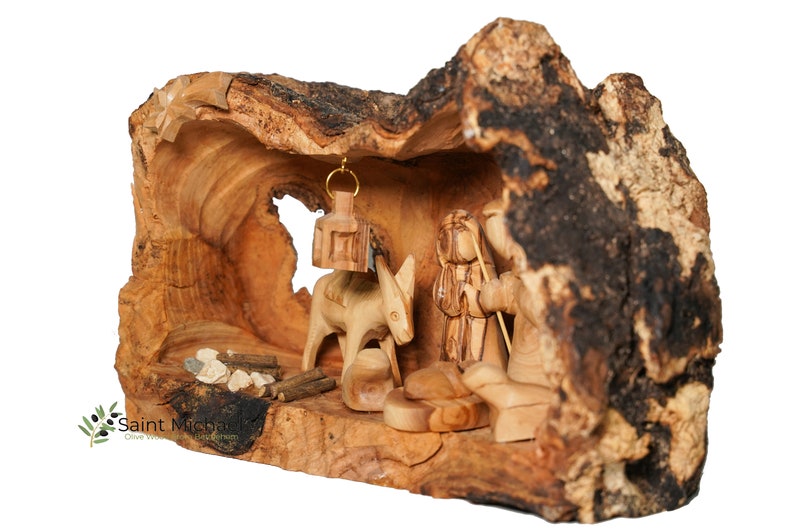 May include: A hand-carved nativity scene set inside a hollowed-out olive wood log. The scene features a donkey, a shepherd, and a small fire.
