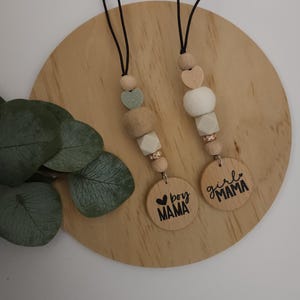 May include: Two wooden keychain charms with black cords. One charm says "boy mama" with a heart and the other says "girl mama". Both charms have a mix of beige, white, and green wooden beads.