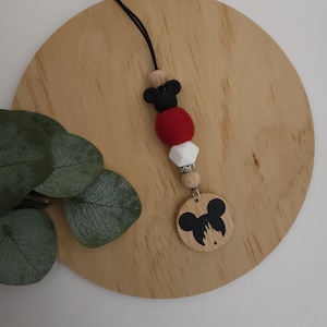May include: A black and white Mickey Mouse themed phone charm with red, white, and wooden beads. The charm features a wooden circle with a black Mickey Mouse head and the iconic Disney castle silhouette.
