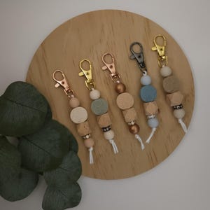 May include: Five wooden bead keychains with different colored beads and metal clasps. The keychains are arranged on a wooden surface.