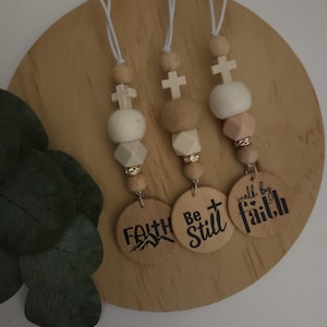 May include: Three wooden bead necklaces with cross charms and wooden round tags with the words "Faith", "Be Still", and "Walk by Faith".