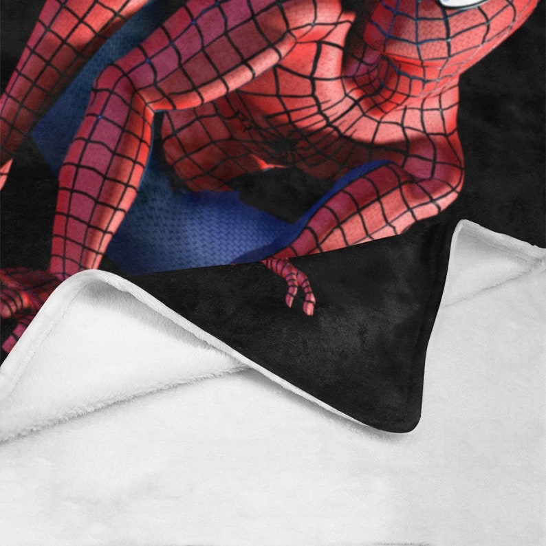 Op de afbeelding: Een zwart en rood fleece deken met een rood en blauw Spiderman ontwerp. Het deken is dubbelgevouwen, waardoor de witte fleece voering zichtbaar is.