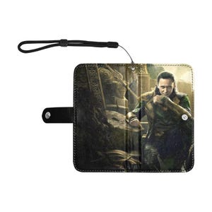 Puede incluir: Funda de cartera negra con un personaje de una película. La funda tiene un cierre magnético y una correa para la muñeca. La imagen de la funda muestra a una persona con un atuendo verde y negro.