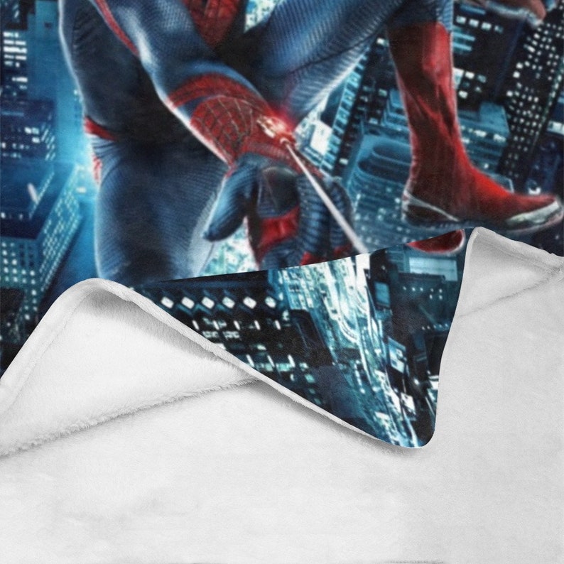 Pu&ograve; includere: Una coperta in pile bianca con un'immagine blu e rossa di Spiderman che si dondola su uno skyline urbano.