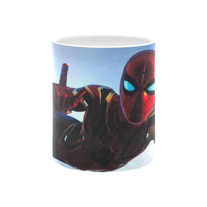 Puede incluir: Una taza de cer&aacute;mica blanca con una imagen colorida de Spider-Man con un traje rojo y dorado, volando por el aire. El fondo es un cielo azul.