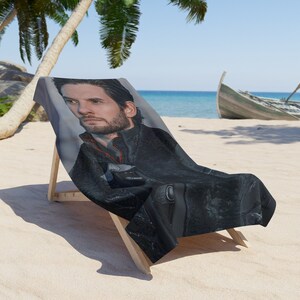 May include: A beach towel with a black and white image of a man with a beard. The man is wearing a black jacket and has a serious expression on his face.