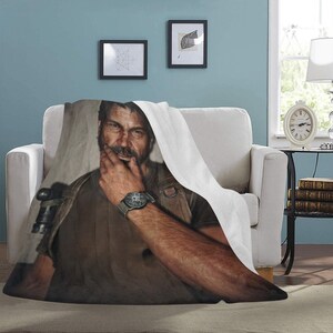 May include: A brown and black fleece blanket with a printed image of a man with a beard and a watch on his wrist. The man is wearing a brown shirt and a black vest.