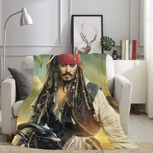Può includere: Una morbida coperta in tessuto con un'immagine in primo piano di Capitan Jack Sparrow della saga cinematografica Pirati dei Caraibi. L'immagine mostra Jack Sparrow con i suoi caratteristici dreadlocks, il bandana rosso e un'espressione maliziosa.