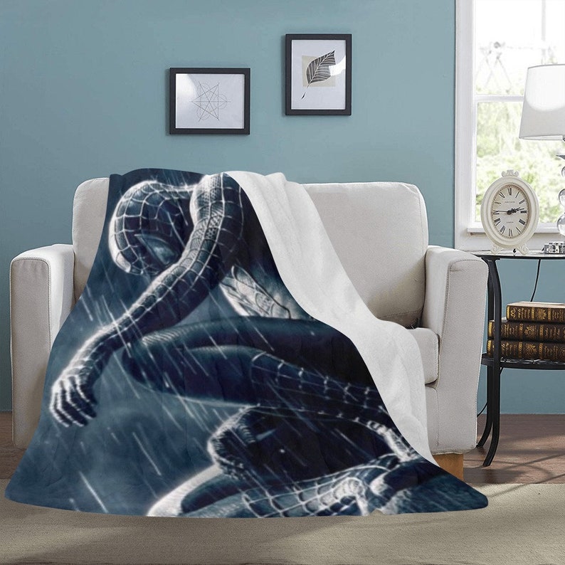 May include: A black and blue fleece blanket with a graphic of a superhero in a dark, rainy setting.