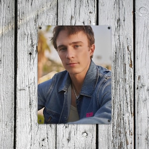 May include: A portrait of a person wearing a denim jacket with the word "GCDS" in pink lettering. The person has light skin, brown hair, and is wearing a silver chain necklace. The background is blurred, with a hint of greenery.