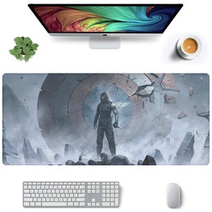 以下が含まれることがあります： グレーとブルーの マウスパッド。壊れたキャプテンアメリカの盾と、その前に立っている人物が描かれている。人物は黒いスーツを着て、銃を持っている。