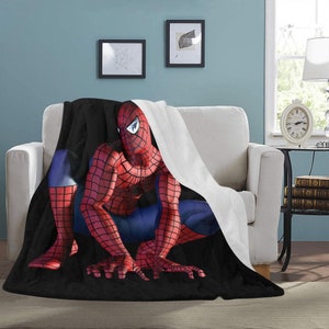 Op de afbeelding: Een zwarte en rode fleece deken met een witte fleece rand heeft een afbeelding van Spiderman die kruipt.