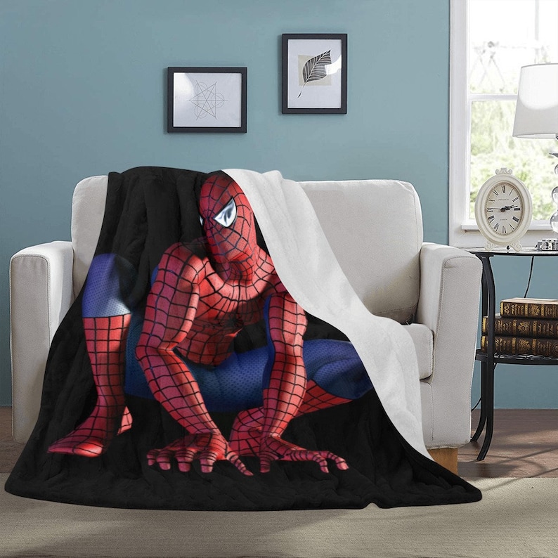 Op de afbeelding: Een zwarte en rode fleece deken met een witte fleece rand heeft een afbeelding van Spiderman die kruipt.