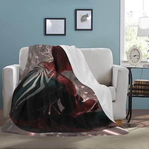 May include: A white fleece blanket with a printed image of Spider-Man in a red and black suit. The image is of Spider-Man's back, with his webbed arms and back visible.