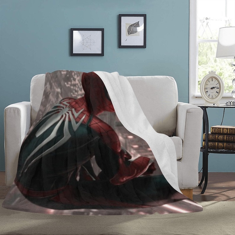 May include: A white fleece blanket with a printed image of Spider-Man in a red and black suit. The image is of Spider-Man's back, with his webbed arms and back visible.