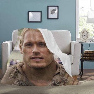 May include: A close-up of a man's face on a white throw blanket. The man has brown hair and brown eyes. He is wearing a brown leather jacket and a white shirt. The blanket is folded over his shoulders.