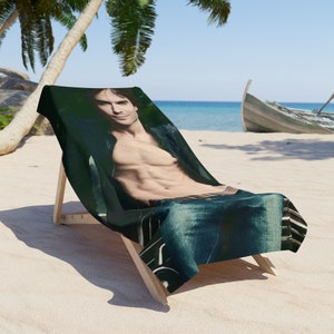 May include: A beach towel with a photo of a shirtless man wearing jeans and a leather jacket. The man is sitting on a beach chair on a sandy beach.