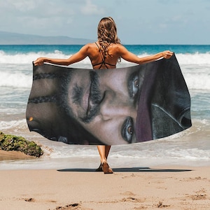 May include: A beach towel featuring a close-up image of a man's face with a black eye patch and braided hair. The towel is draped over a person's shoulders.