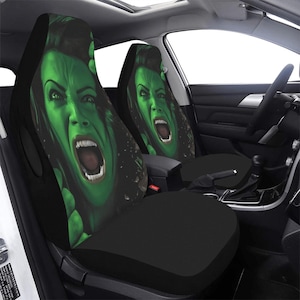 May include: A pair of black car seat covers with a green and black graphic print of a woman with a fierce expression. The woman's face is contorted in a scream.