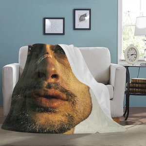 May include: A close-up of a man's face with a bandage on his nose. The image is printed on a white throw blanket.