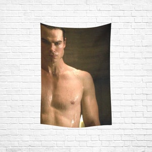 May include: A shirtless man with wet hair and a muscular physique stands in a dimly lit room. Water droplets are visible on his skin.