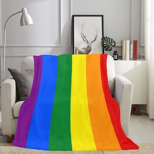 Puede incluir: Una manta de tiro a rayas de arcoíris con un esquema de color morado, azul, verde, amarillo, naranja y rojo. La manta está drapeada sobre un sofá.