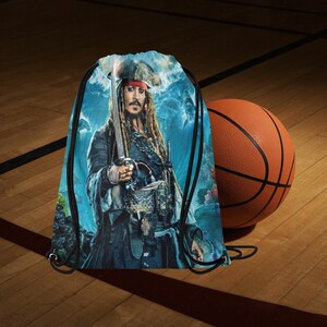 May include: A blue drawstring bag with a graphic of Captain Jack Sparrow from the Pirates of the Caribbean movie franchise. The bag has a white drawstring and black accents.