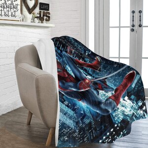 Pu&ograve; includere: Una morbida e soffice coperta in pile con un'immagine vibrante di Spider-Man che si dondola su uno skyline notturno di citt&agrave;. La coperta &egrave; bianca sul lato opposto.