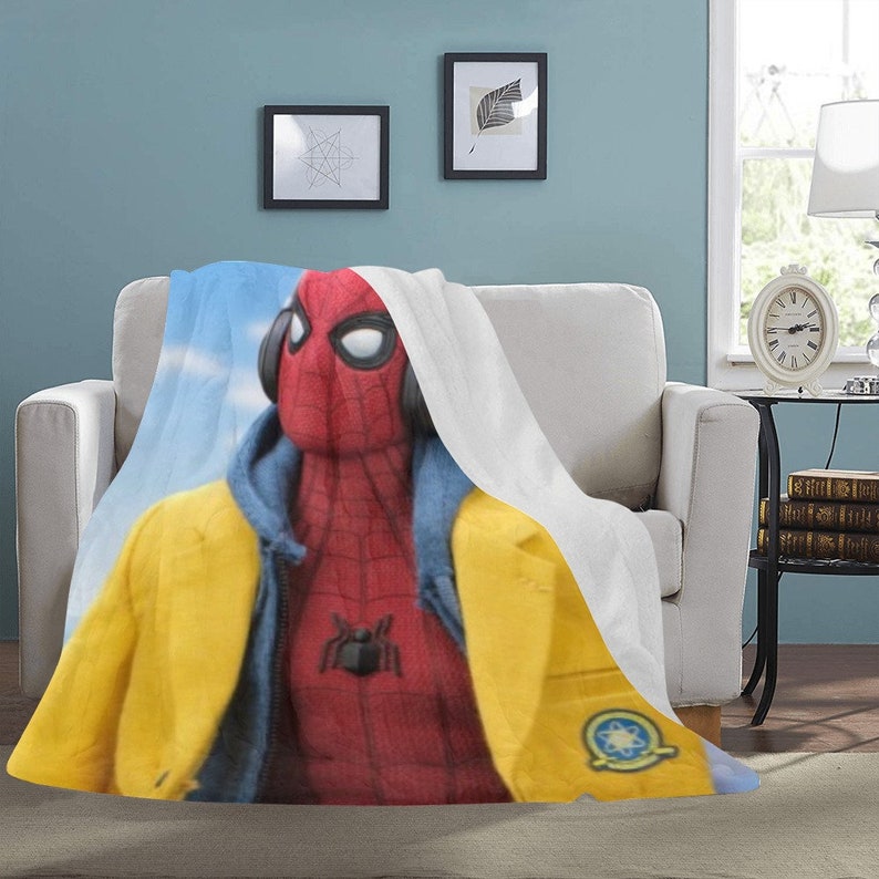 May include: A red and blue superhero character wearing a yellow jacket and a blue hoodie. The character is wearing headphones and has a spider symbol on their chest. The character is on a white and blue blanket.