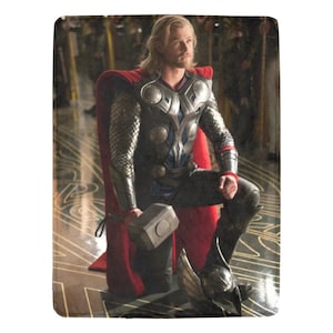 May include: A superhero character wearing a red cape and silver armor, holding a silver hammer. The character has long blonde hair and is kneeling on a patterned floor.