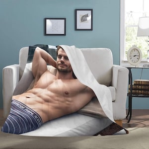 May include: A white blanket with a man lying on top of it. The man is wearing striped underwear and has a bare chest. The blanket is on a white couch.