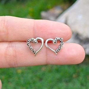 Könnte beinhalten: Ein Paar silberne herzförmige Ohrringe mit einem Rand aus kleinen, dunkelgrauen Steinen.