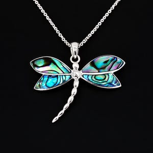 May include: A silver dragonfly pendant necklace featuring iridescent abalone shell inlays within the wings. The dragonfly has a segmented silver tail and is suspended from a delicate silver chain, showcasing vibrant blue, green, and purple hues.