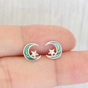 以下が含まれることがあります： 星が中央に付いた、三日月型のシルバーのイヤリングのペア。月は緑色のアワビの貝殻で作られています。