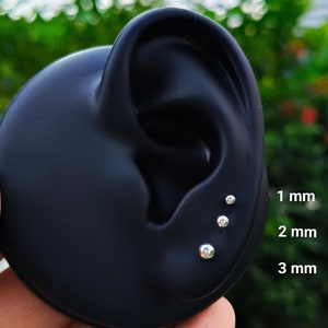May include: A black ear model with three silver stud earrings. The earrings are 1 mm, 2 mm, and 3 mm in size.