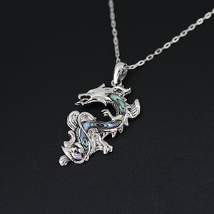 May include: A silver dragon pendant necklace with iridescent abalone shell inlay. The dragon is detailed with scales and a fierce expression, suspended from a delicate chain. The pendant is approximately 2 inches in length.