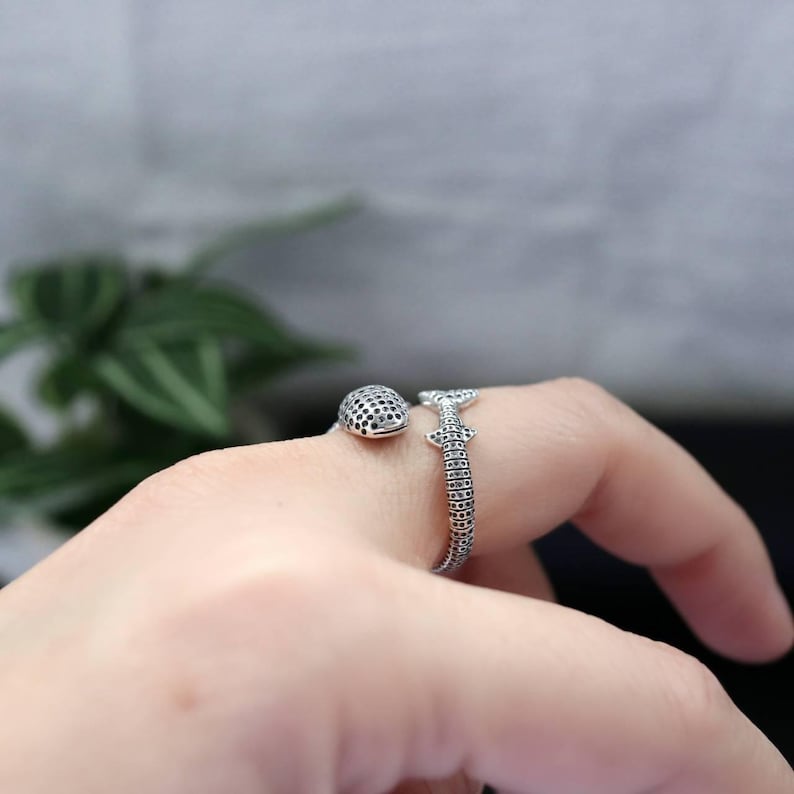 K&ouml;nnte beinhalten: Ein silberner Ring mit Wal- und Hai-Design. Der Wal hat eine strukturierte Oberfl&auml;che mit kleinen schwarzen Punkten, und der Hai hat einen strukturierten K&ouml;rper. Der Ring wird an einem Finger getragen. Der Ring ist aus Silber.