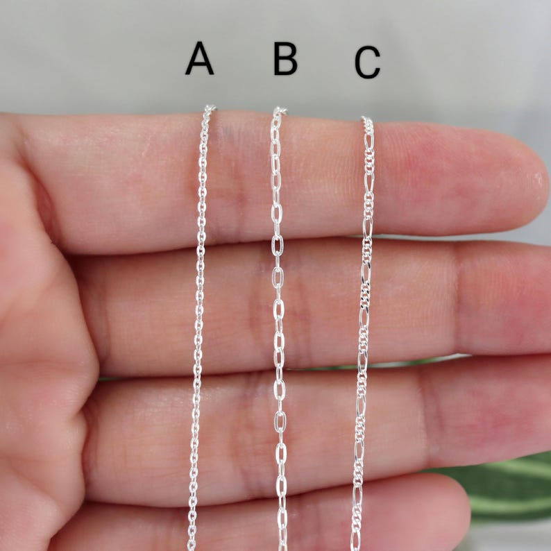 May include: Three silver chain necklaces, labeled A, B, and C, are displayed. Chain A is a delicate cable chain, B is an oval link chain, and C is a Figaro chain. The chains are shown against a neutral background.