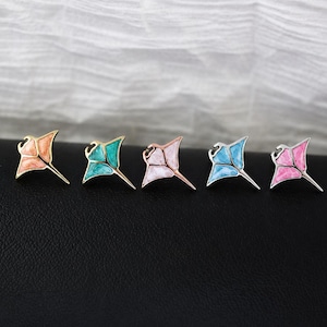 May include: Five stingray-shaped pins arranged in a row. Each pin features a metallic outline filled with marbled enamel in distinct colors: peach, teal, light pink, light blue, and bright pink. The pins have a pointed tail and wing-like fins.