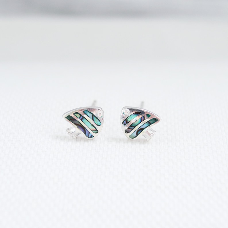 May include: A pair of silver stud earrings featuring a blue and green abalone shell design in the shape of a fish.