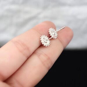 May include: A pair of silver-colored stud earrings. Each earring features a gear-like design with small, pointed teeth around the edge. The earrings are held in place by a post and butterfly clasp.