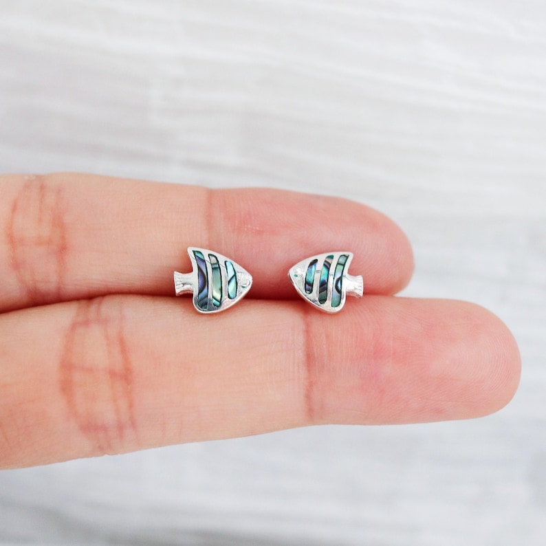 May include: A pair of silver fish-shaped earrings with iridescent blue and green abalone shell inlays.