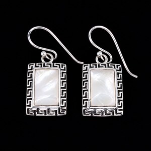 May include: A pair of rectangular drop earrings featuring a central iridescent white mother-of-pearl inlay. The silver-toned metal frame is decorated with a repeating Greek key pattern. Each earring hangs from a curved silver-toned ear wire hook.