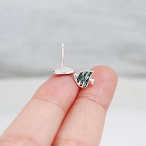 May include: A pair of silver stud earrings featuring a small, green and white fish design. The fish is made of mother-of-pearl.